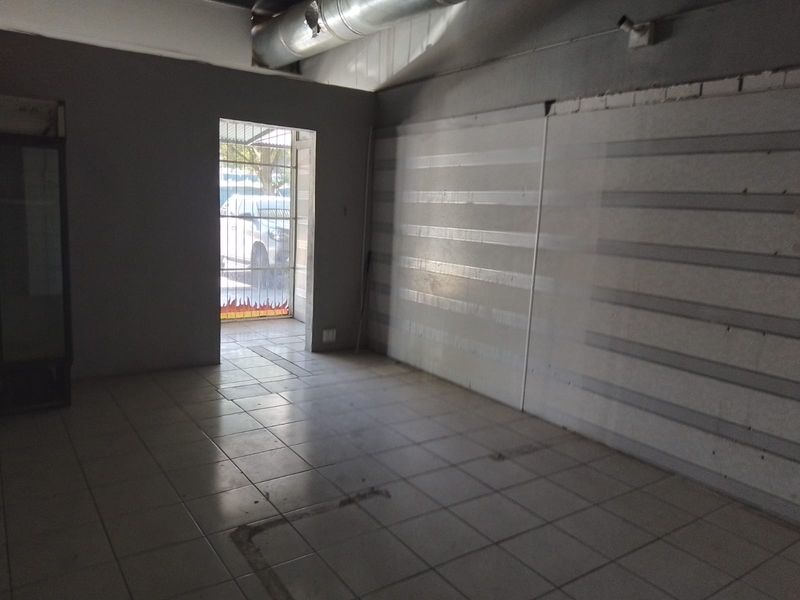 Empty retail space featuring tiled flooring, exposed industrial ducting, and wall-mounted slatwall display panels with a secure entrance.