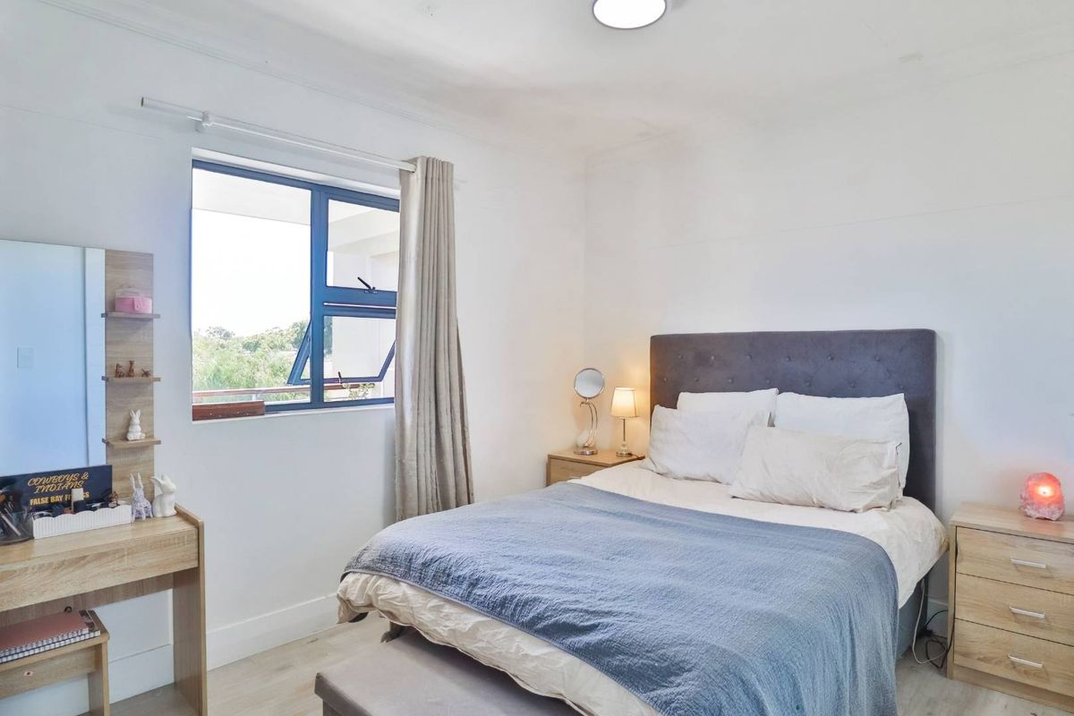 A bright and well-maintained bedroom featuring neutral walls, light-toned flooring, and a large window that allows for ample natural light.