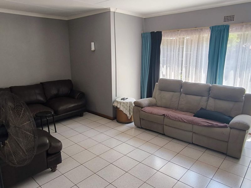 A spacious living room featuring neutral grey walls, ceramic tiled flooring, and a large sliding glass door providing natural light and garden access.