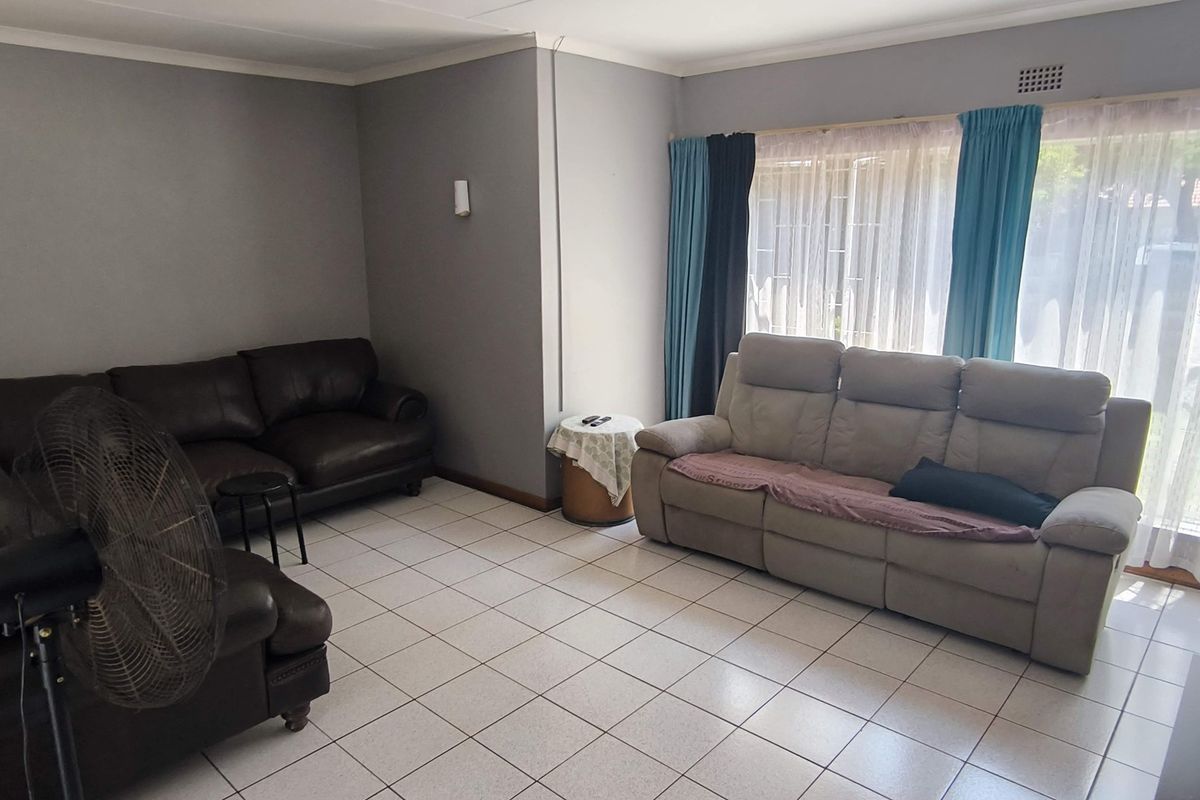 A spacious living room featuring neutral grey walls, ceramic tiled flooring, and a large sliding glass door providing natural light and garden access.