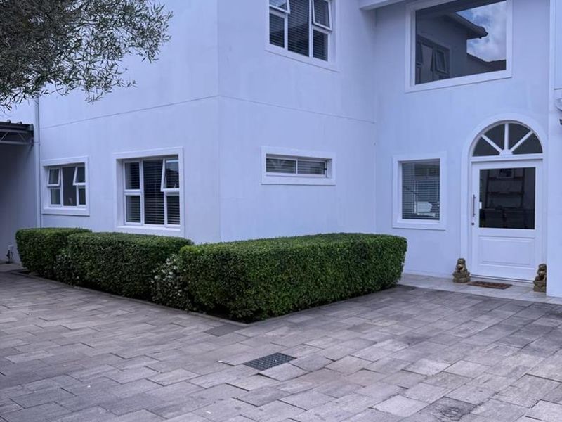 Front elevation of a two-story residence featuring a paved driveway, manicured hedging, and a prominent arched entrance door.