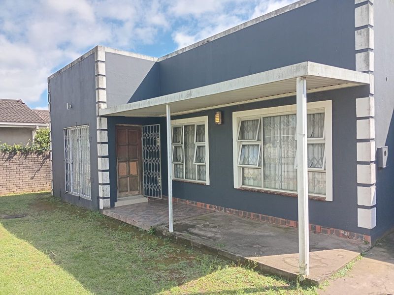 Front elevation of a house featuring a covered patio, security gates, and metal window frames, showing signs of exterior wear and weathering.