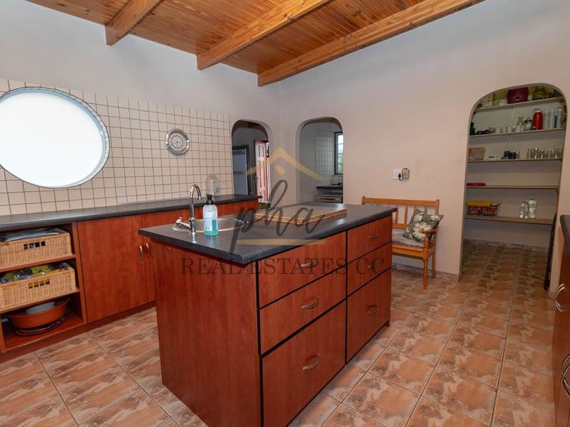 A functional kitchen featuring a central island, ample built-in cabinetry, a walk-in pantry, and distinctive exposed timber beam ceilings.