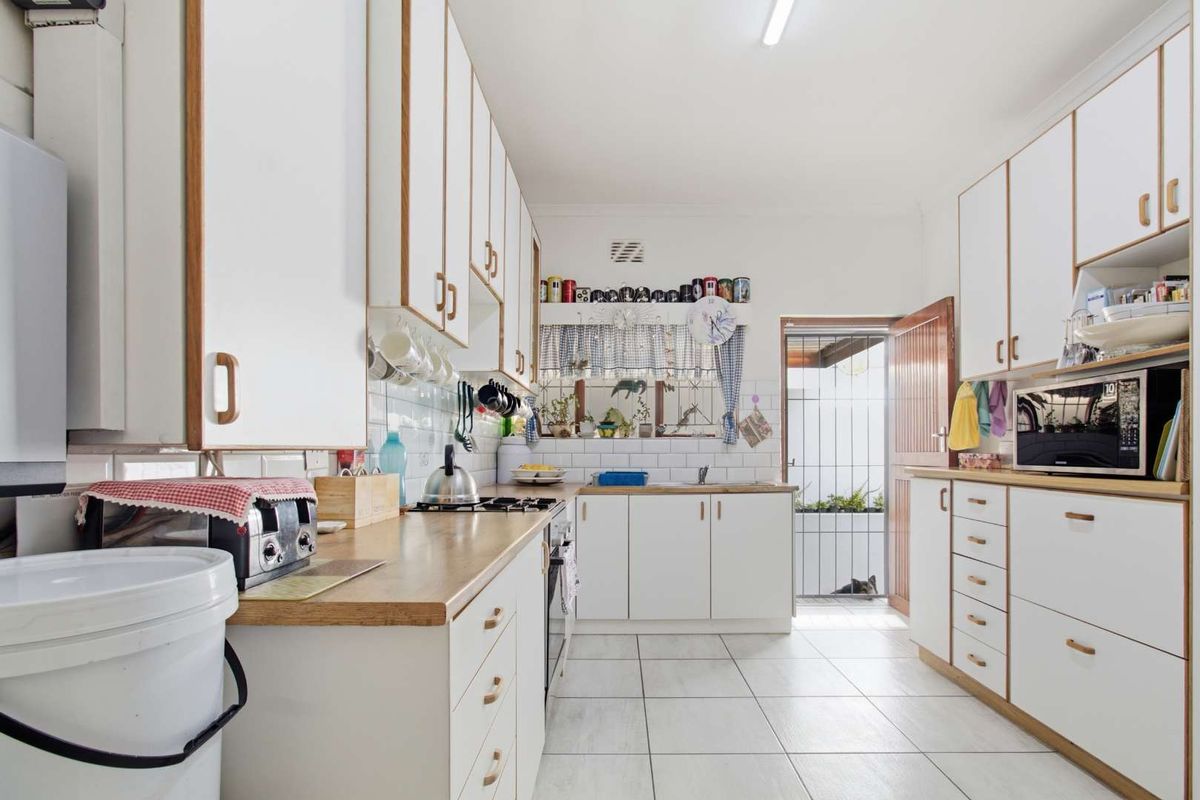 A functional kitchen featuring white cabinetry, wood-look laminate countertops, tiled backsplash, and ceramic floor tiles with direct access to the rear exterior.