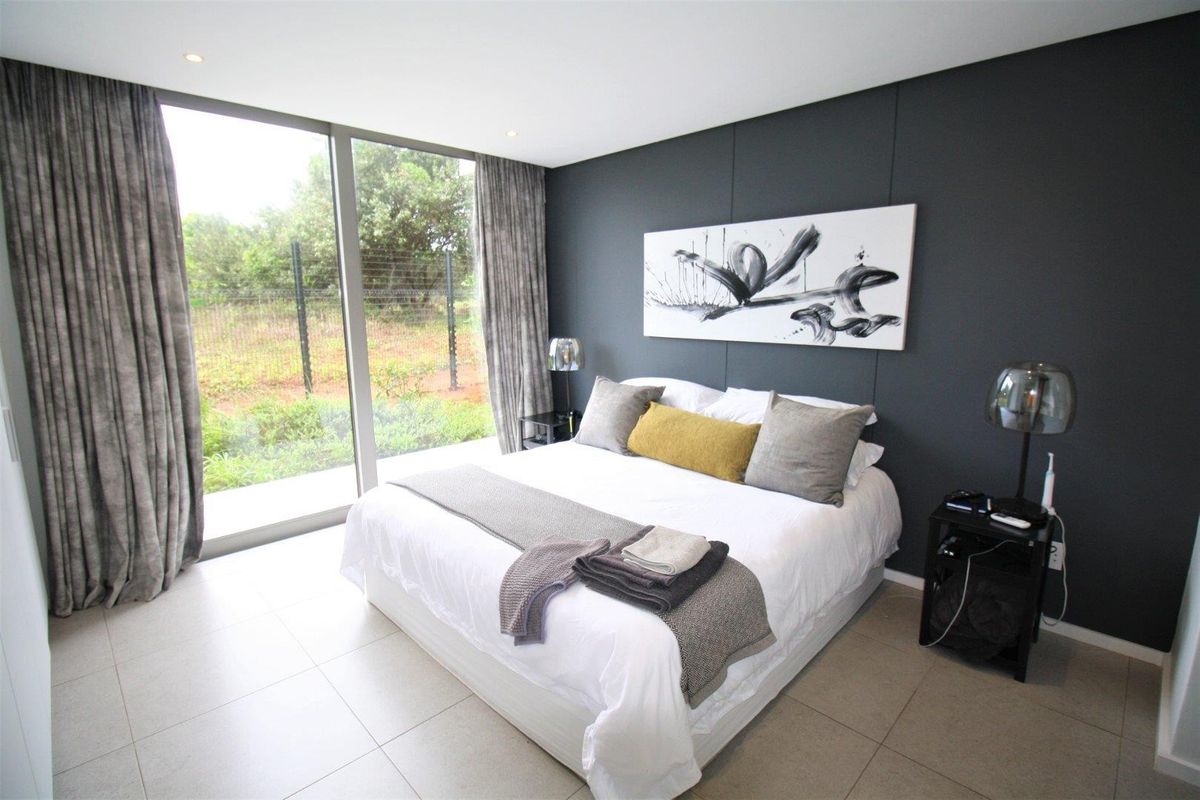 Modern bedroom featuring large floor-to-ceiling windows, neutral tiled flooring, and a dark feature wall, offering a bright and contemporary living space.