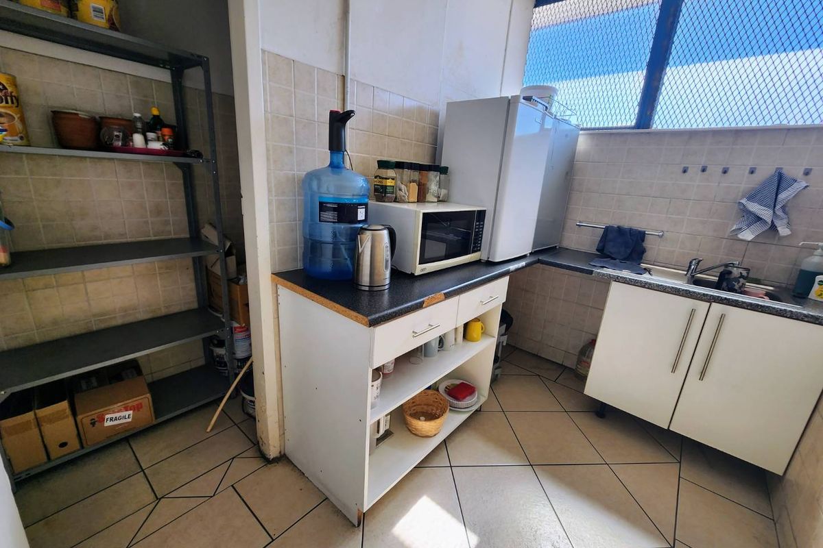 A functional kitchenette area featuring tiled walls, a stainless steel sink, laminate countertops, and built-in base cabinetry with an adjacent storage shelving unit.