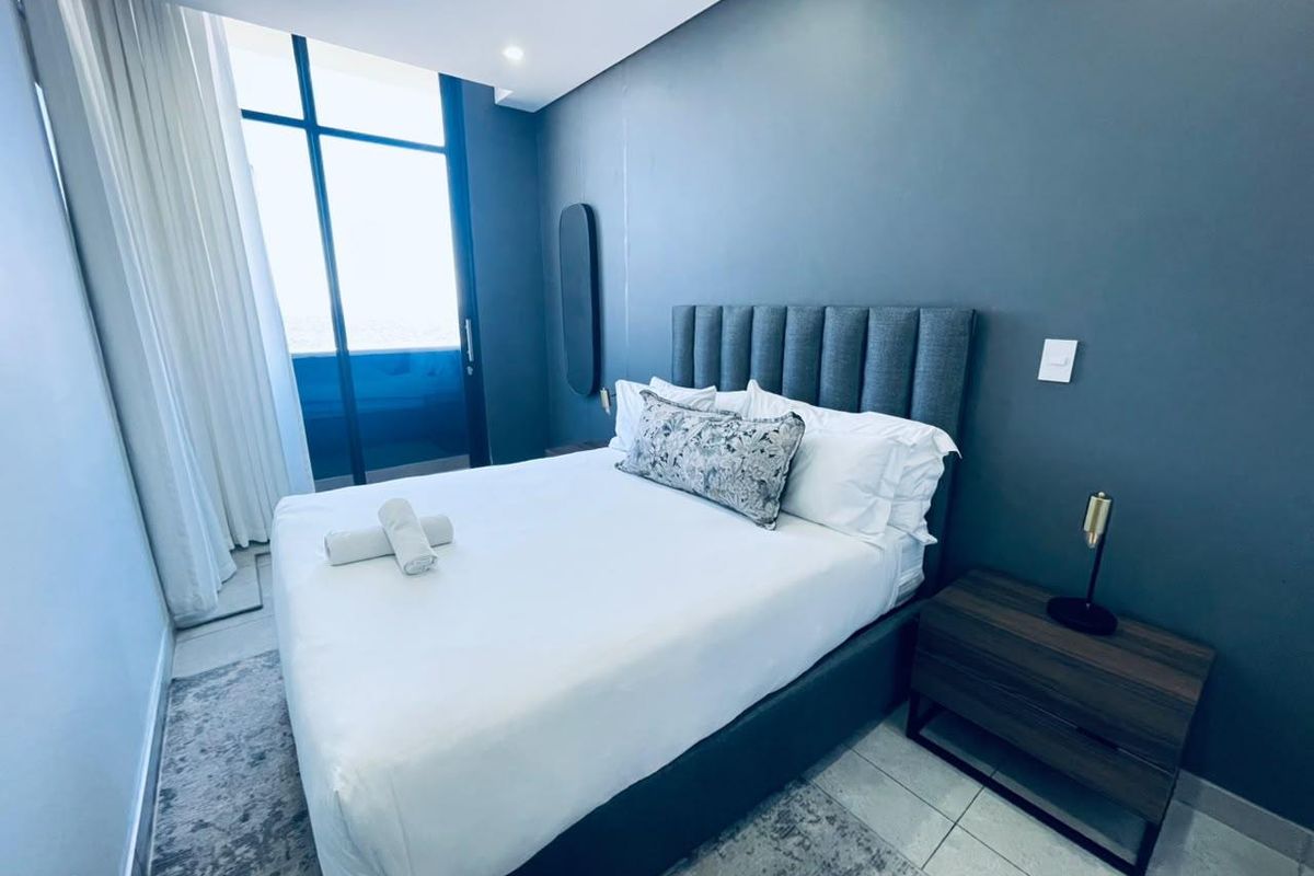 Modern bedroom featuring dark accent walls, recessed lighting, and large glass sliding doors providing access to an outdoor balcony area.