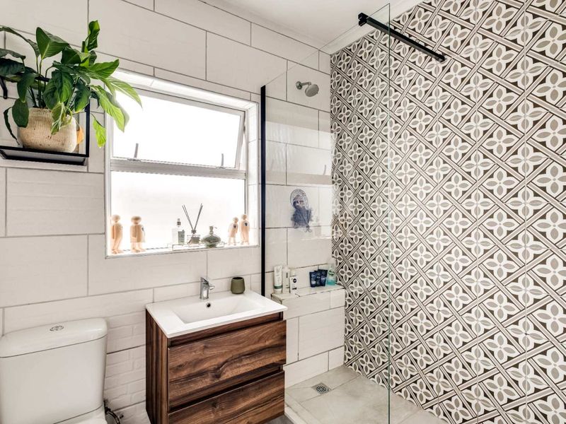 Modern bathroom featuring a wood-finish vanity, patterned feature wall, glass shower enclosure, and white subway-style wall tiles.