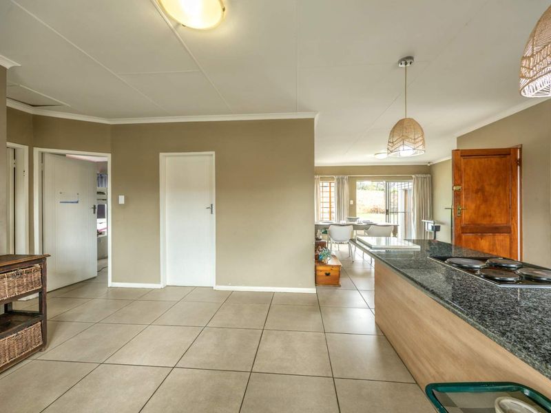 Spacious open-plan living and kitchen area featuring tiled flooring, a granite-topped kitchen island with a built-in hob, and neutral wall tones.