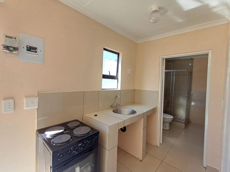 A compact kitchen area featuring a tiled countertop, stainless steel sink, and electric stove, with direct access to an adjoining bathroom.
