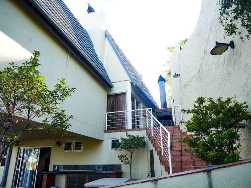 Rear exterior view featuring a tiled staircase with metal balustrades, an outdoor fireplace, and access to the upper level of the property.
