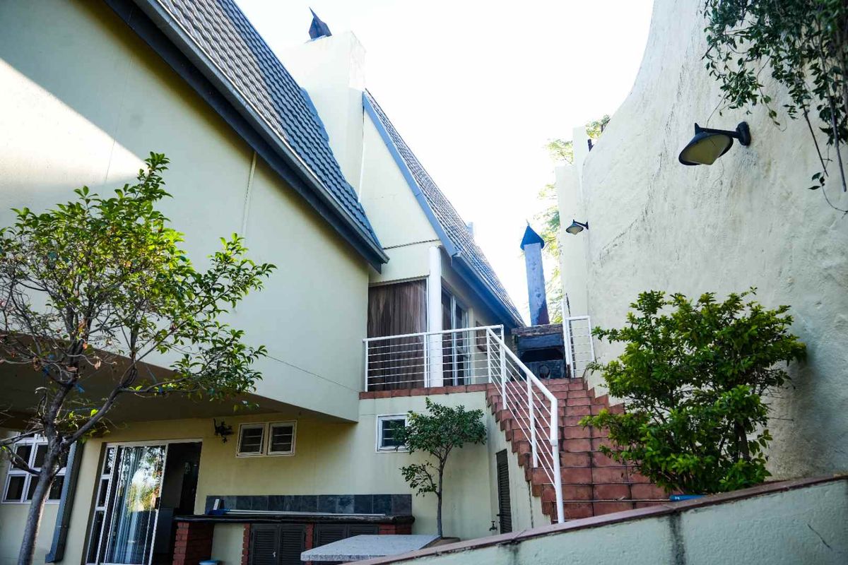 Rear exterior view featuring a tiled staircase with metal balustrades, an outdoor fireplace, and access to the upper level of the property.