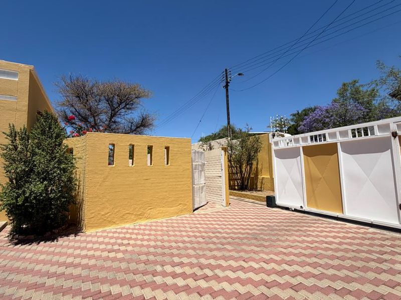 A well-maintained front entrance area featuring a paved driveway, secure sliding gate, and a decorative boundary wall.
