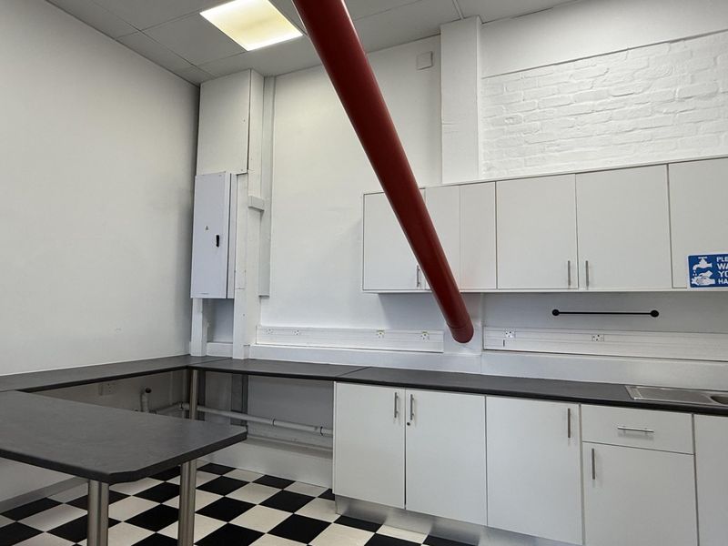 A functional office kitchenette featuring white cabinetry, dark laminate countertops, a stainless steel sink, and a distinctive checkerboard floor pattern.