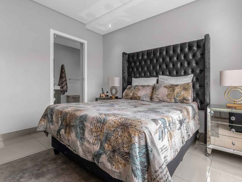 A well-maintained bedroom featuring neutral wall tones, recessed ceiling lighting, and tiled flooring, with an adjoining bathroom visible through the doorway.