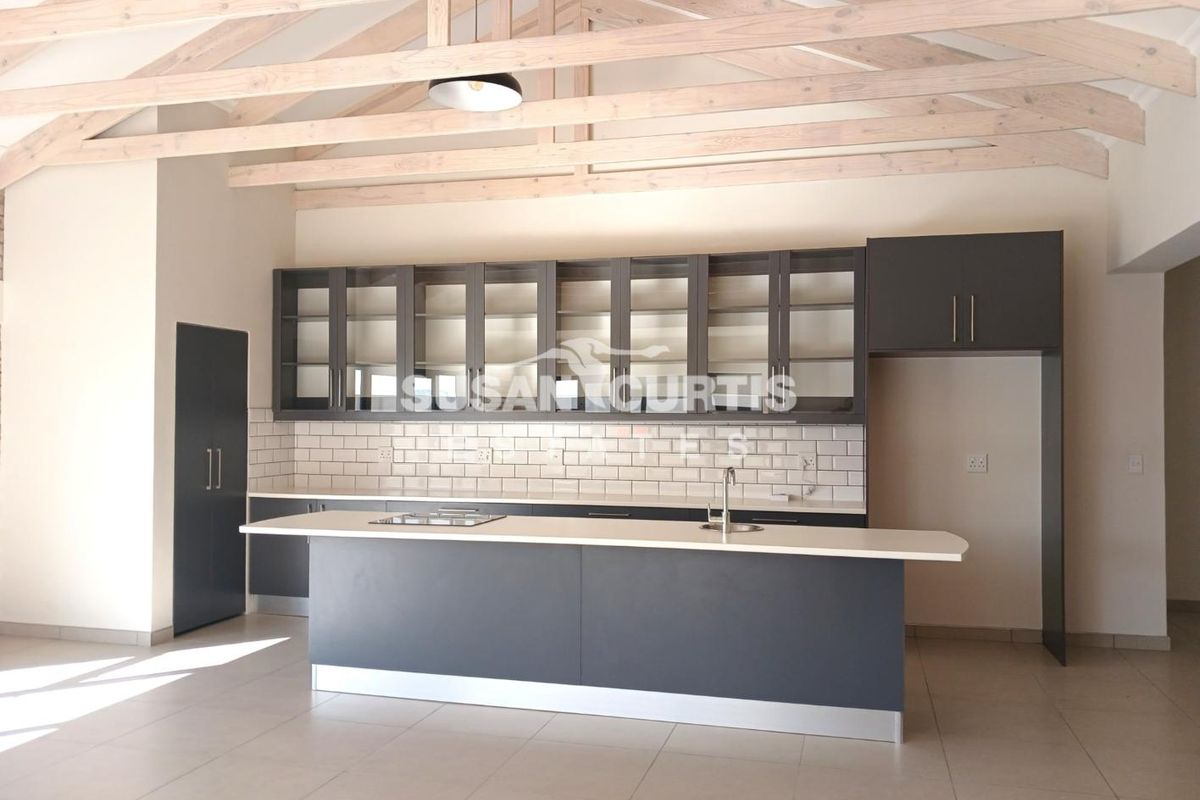 Modern kitchen featuring dark cabinetry, a central island with a sink, subway tile backsplash, and exposed timber roof trusses.
