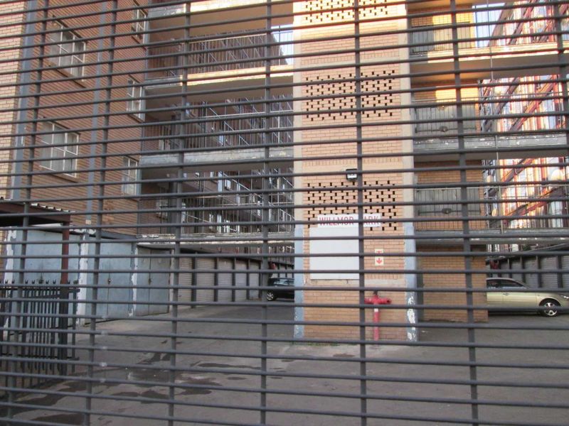 Exterior view of an apartment complex featuring a brick facade, multiple balconies, and a secure gated entrance with garage access.