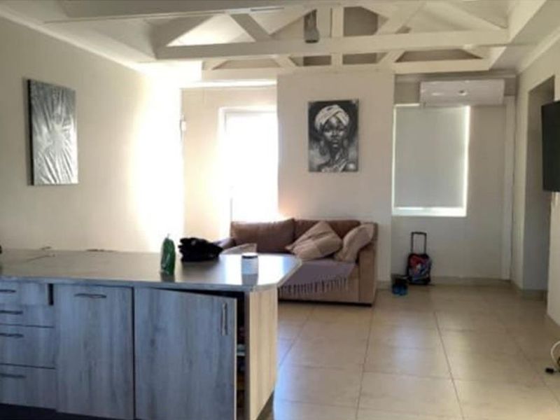 Open-plan living area featuring a kitchen island, tiled flooring, and exposed ceiling beams, with an integrated air conditioning unit.