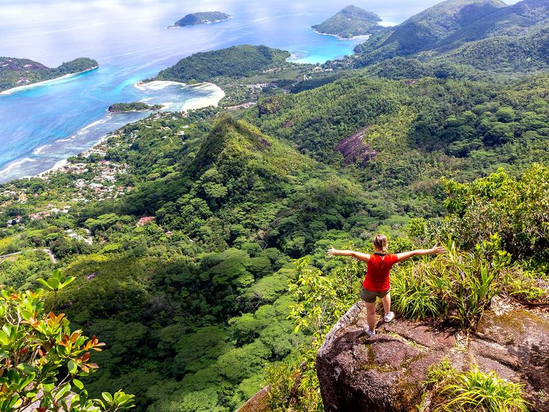 A breathtaking elevated aerial view overlooking lush tropical mountains, coastal forests, and the turquoise ocean waters of the surrounding landscape.