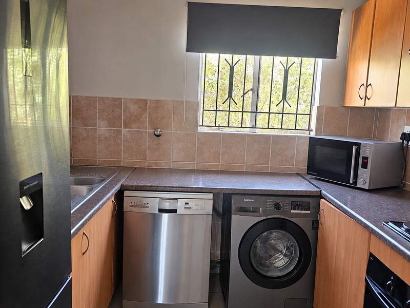 A functional kitchen featuring laminate cabinetry, tiled backsplash, integrated appliances, and a window with security bars for added safety.
