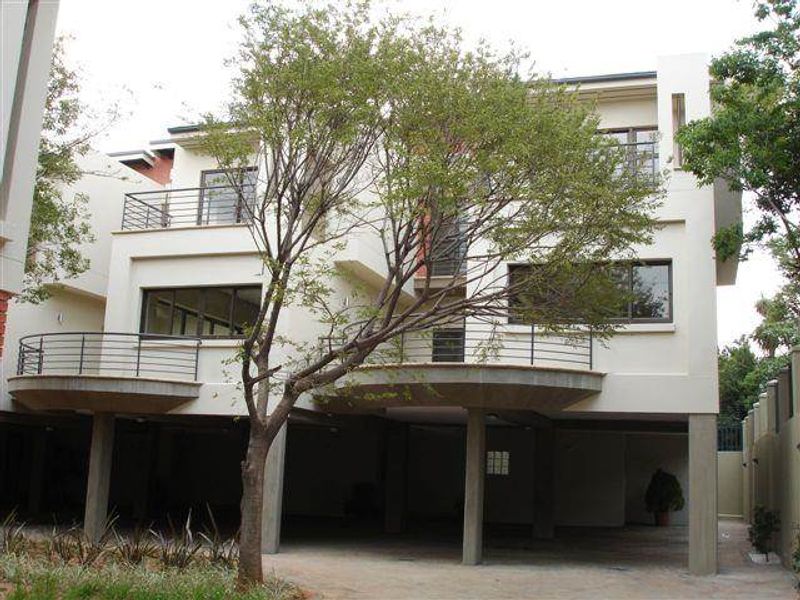 Rear elevation of a multi-story townhouse featuring elevated balconies with metal railings, large windows, and a covered ground-level parking area.