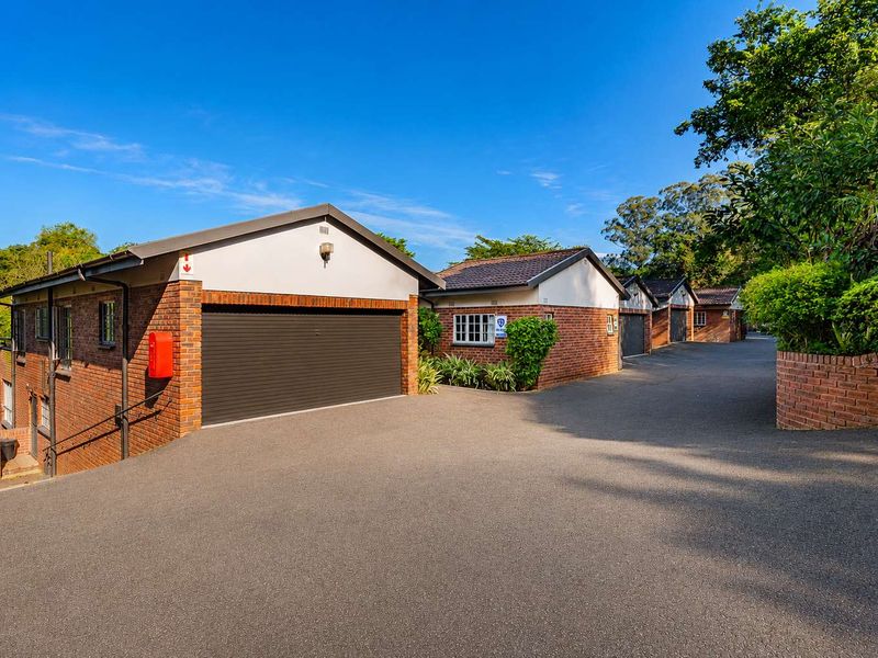 Exterior view of a townhouse complex featuring brick facades, multiple roller garage doors, and a well-maintained asphalt driveway.