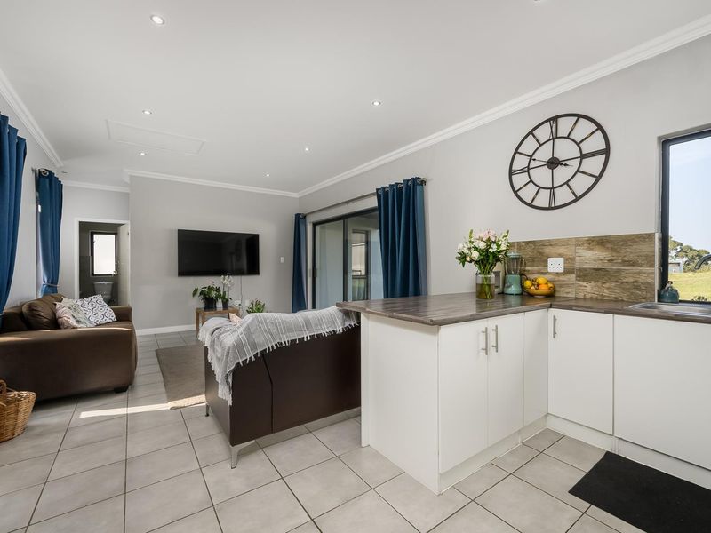 Open-plan living area featuring a modern kitchen with white cabinetry, laminate countertops, tiled flooring, and direct access to the outdoor space via sliding doors.