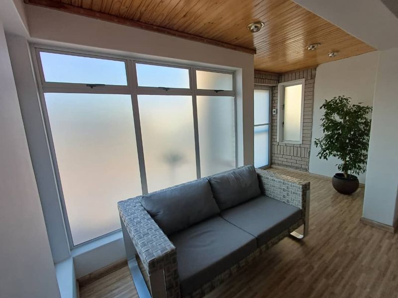 A bright, enclosed patio area featuring a warm timber ceiling, frosted glass windows, and a textured brick feature wall.