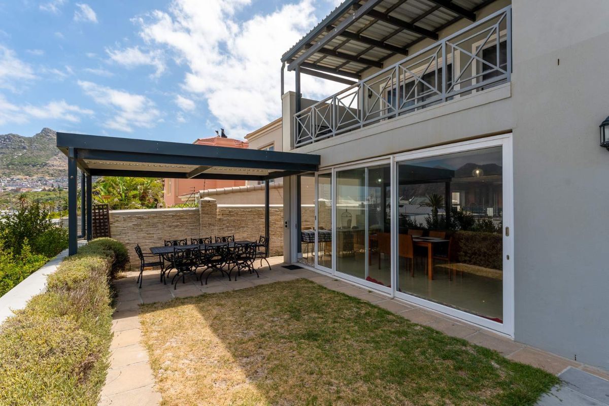 Rear exterior view featuring a covered patio area, a small lawn, and a balcony with metal railings overlooking the garden.
