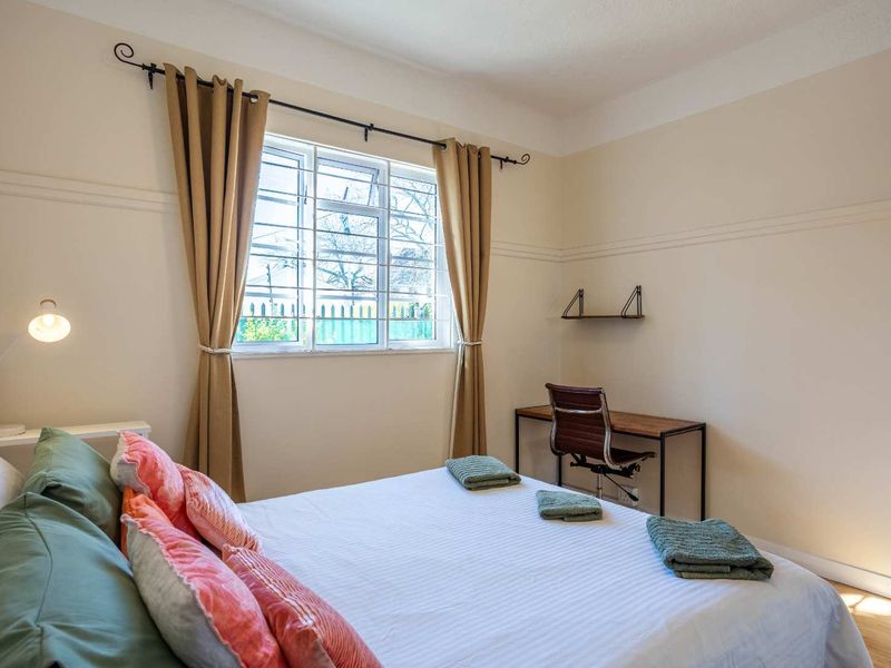 A well-lit bedroom featuring timber flooring, a window with security bars, and classic picture rail detailing.
