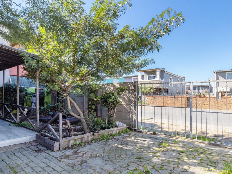 Front exterior area featuring a paved driveway, metal security gate, and a covered patio space with timber decking and boundary walling.