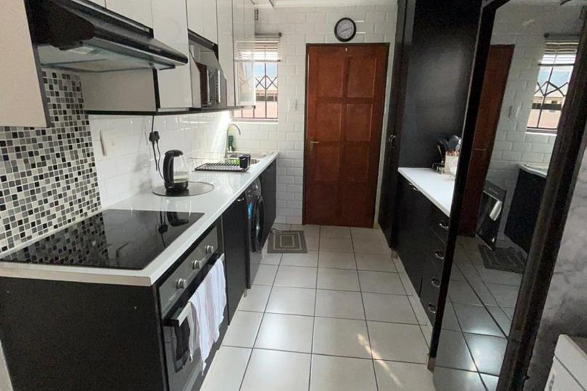 Modern galley-style kitchen featuring sleek black and white cabinetry, integrated oven, hob, extractor fan, and tiled flooring.