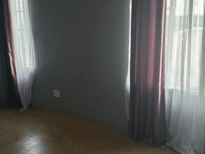 An empty bedroom featuring vinyl flooring, dual windows with curtains, and a ventilation grille, offering a blank canvas for renovation.