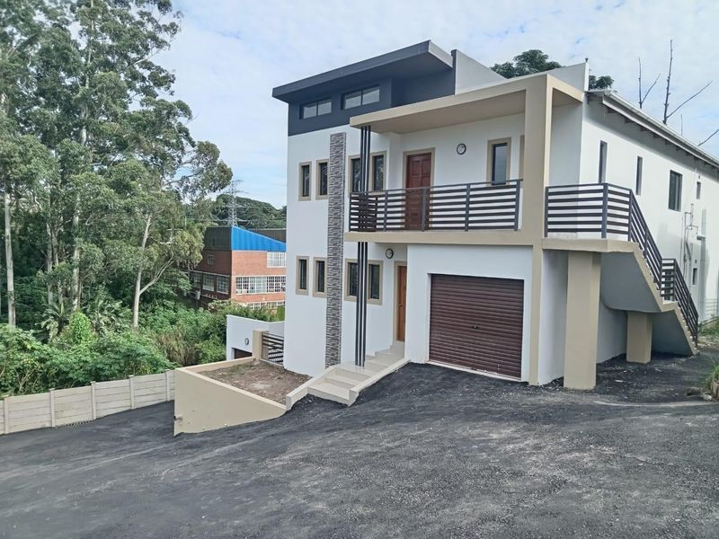 Modern three-story townhouse featuring a roller garage door, an upper-level balcony with metal railings, and an external staircase, set on a paved driveway.