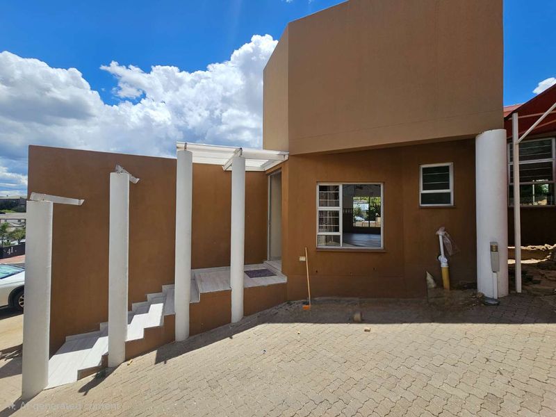Front exterior view of the property featuring a paved driveway, tiled staircase with structural columns, and aluminium window frames.