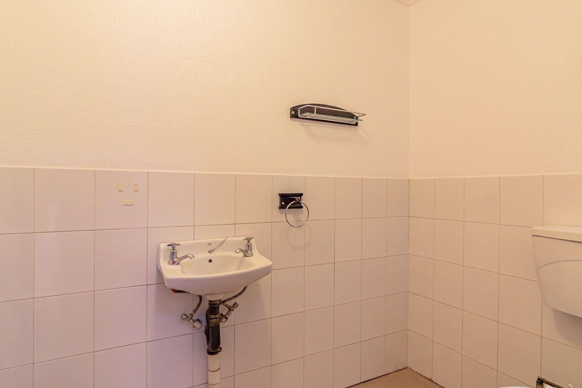 A functional office restroom featuring a wall-mounted basin, standard toilet, and white tiled walls.