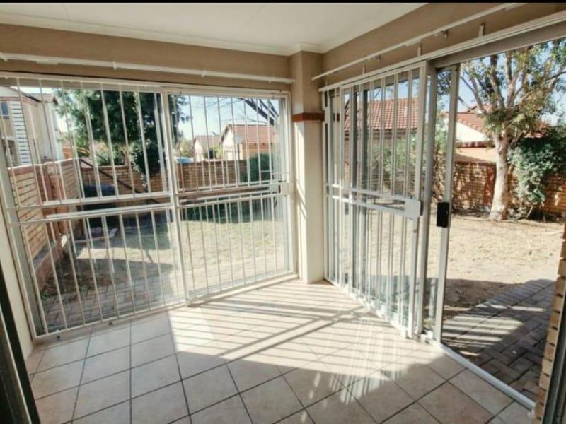 Enclosed patio area featuring tiled flooring and sliding glass doors with security gates, providing direct access to the rear garden space.