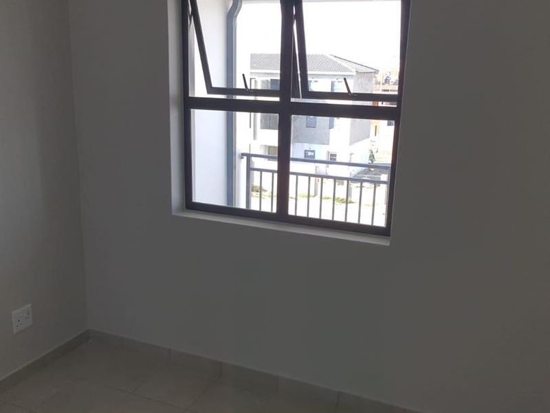 A clean, empty bedroom featuring neutral tiled flooring and a modern aluminium window frame with an installed curtain rail.