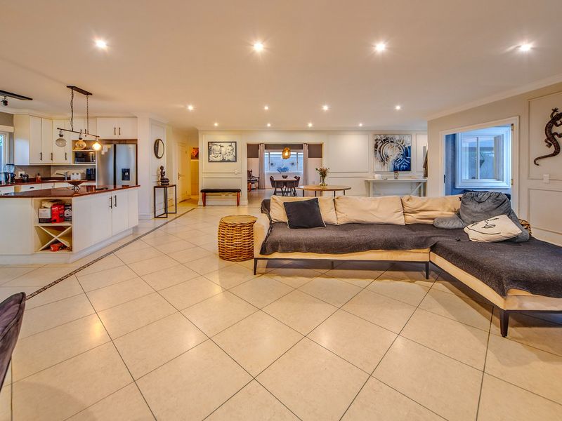 Spacious open-plan living area featuring a modern kitchen with a central island, tiled flooring, and recessed lighting, seamlessly flowing into the dining and lounge spaces.