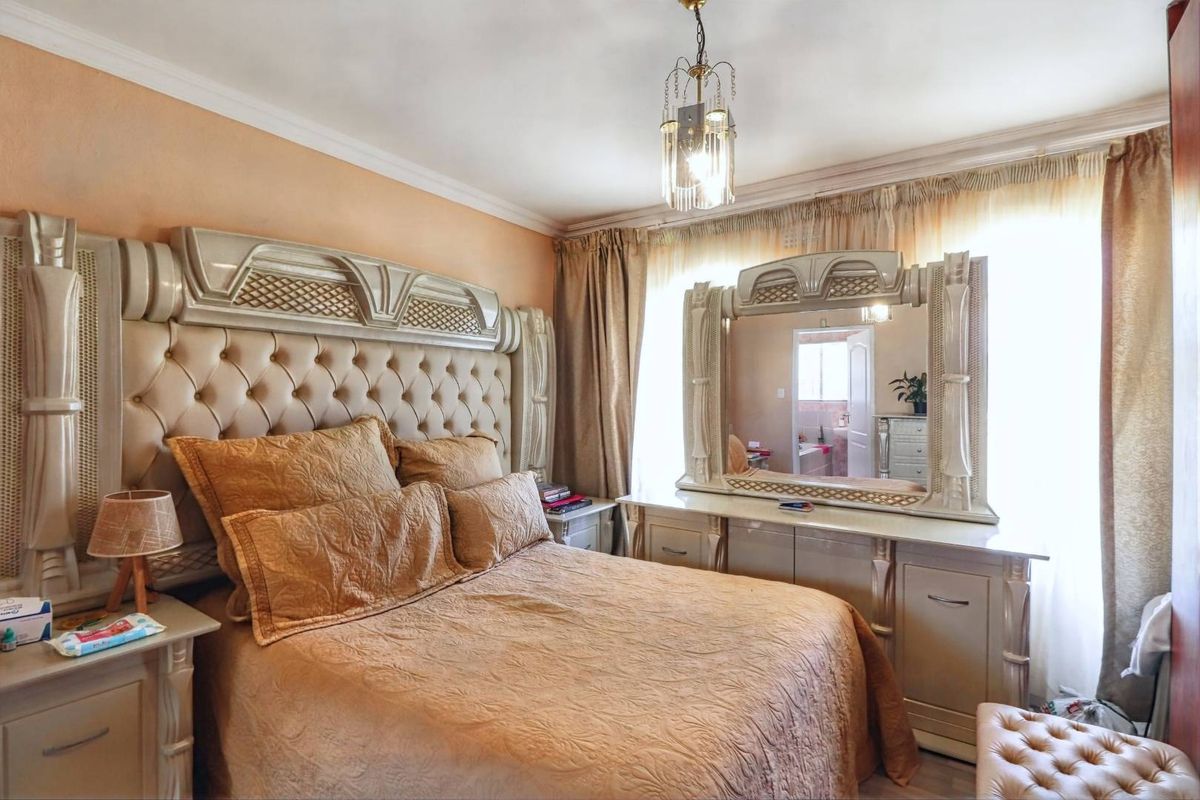 A well-maintained bedroom featuring crown molding, a central pendant light fixture, and large windows with integrated curtain tracks.