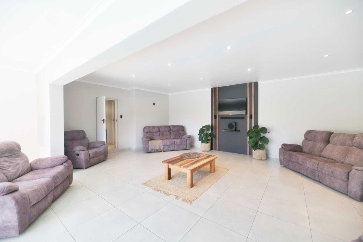 Spacious living room featuring neutral tiled flooring, recessed downlighting, and a modern decorative feature wall panel.