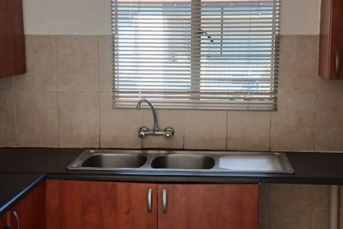 A functional kitchen area featuring laminate cabinetry, a double bowl stainless steel sink, ceramic tile splashbacks, and tiled flooring.
