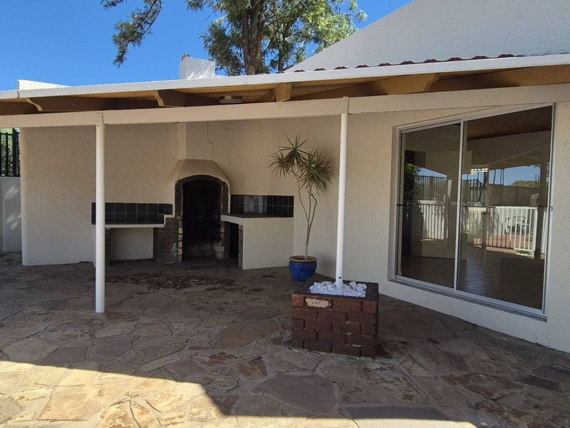 Covered outdoor patio area featuring a built-in braai, stone paving, and direct access to the interior through a sliding glass door.