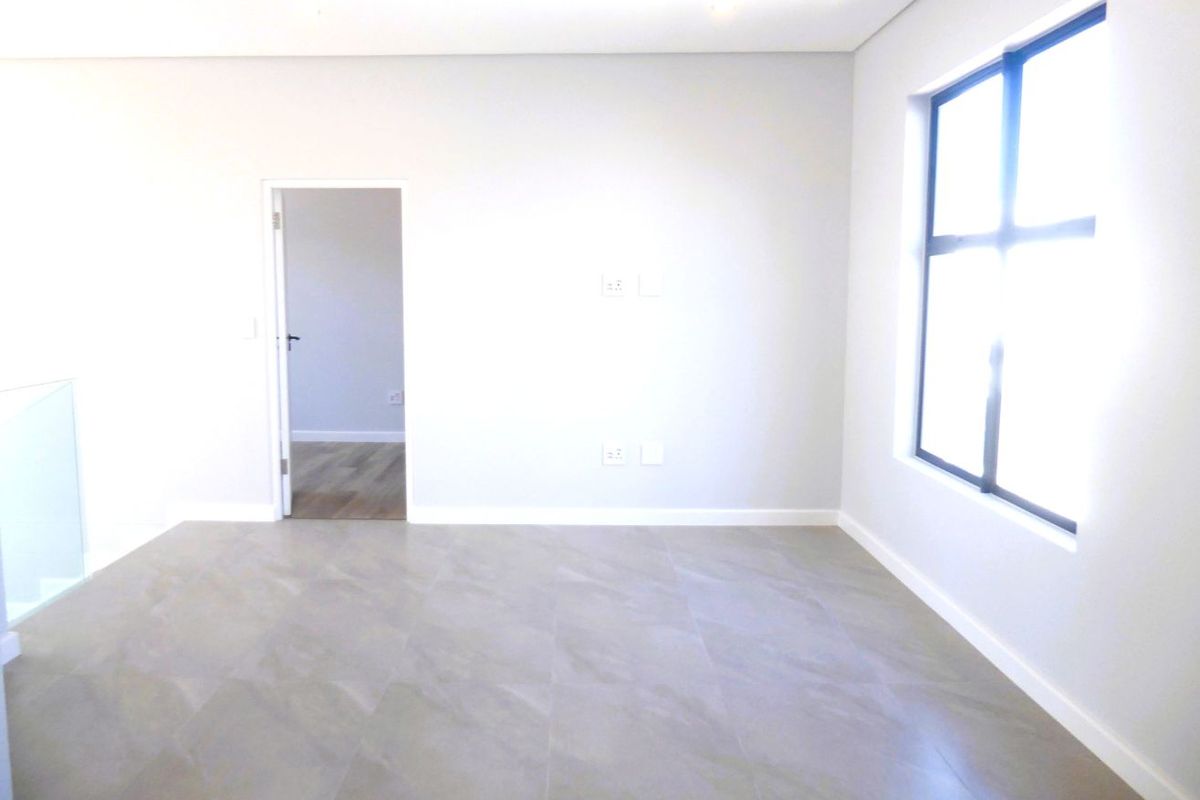 A bright, modern, and empty bedroom featuring neutral tiled flooring, clean white walls, and large aluminium-framed windows allowing for ample natural light.
