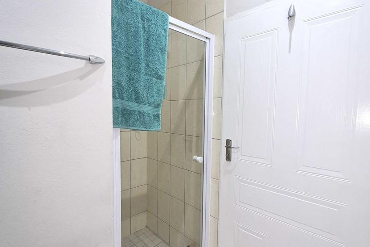 A compact bathroom featuring a tiled shower enclosure with a glass door, white panel door, and neutral floor tiling.
