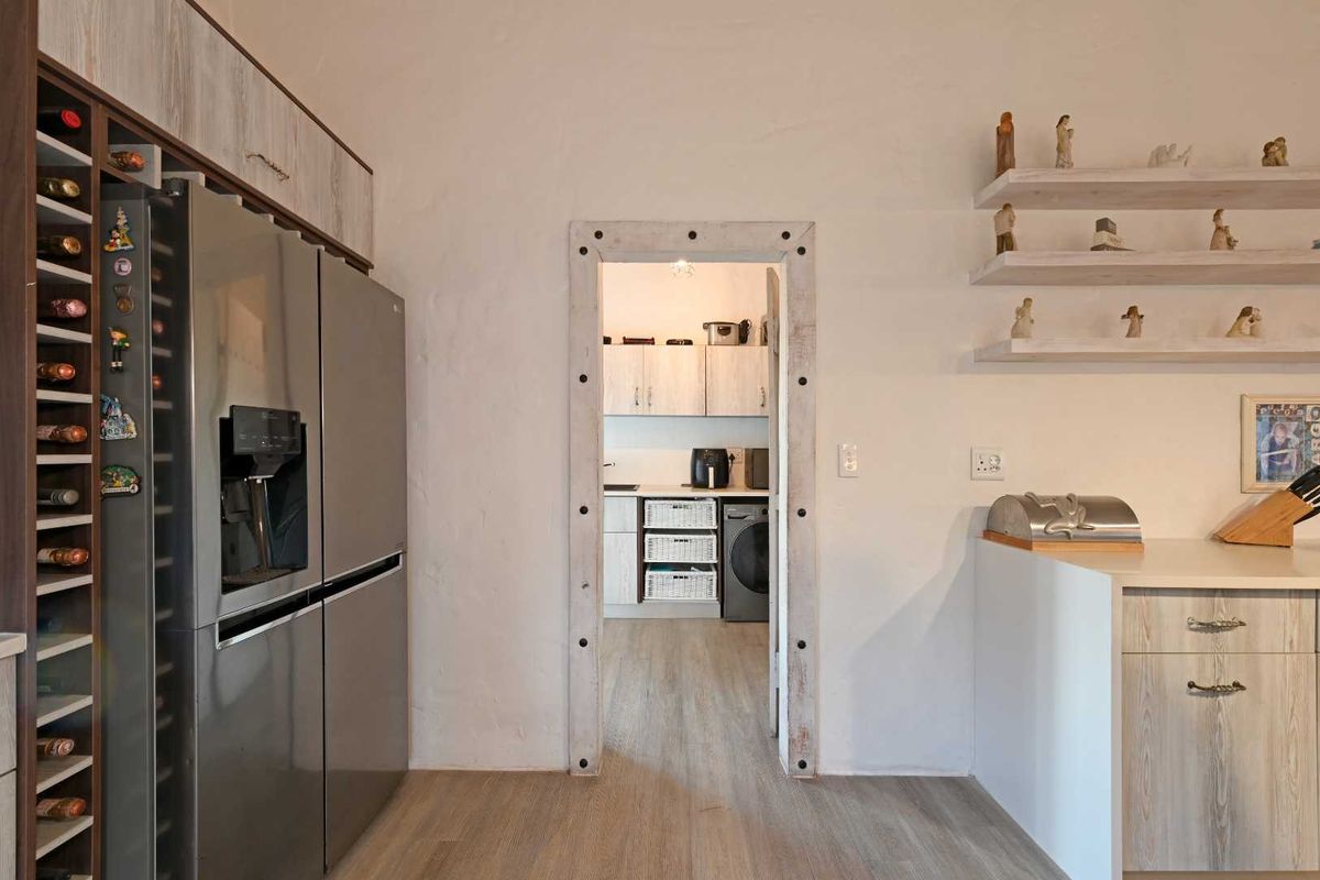 A view from the kitchen into a functional scullery area, featuring modern cabinetry, wood-look flooring, and a built-in wine rack.
