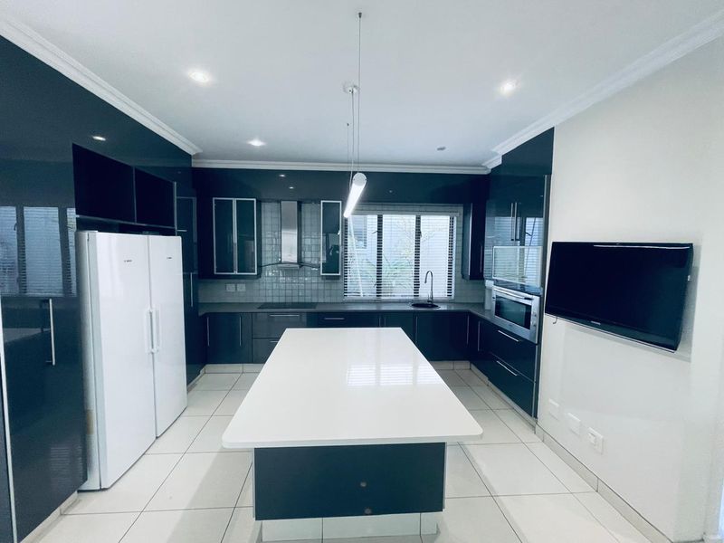Modern kitchen featuring high-gloss cabinetry, a central island with stone countertop, built-in appliances, and tiled flooring.
