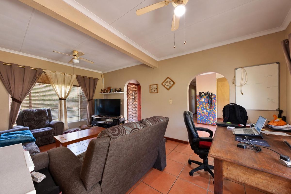 A spacious living area featuring tiled flooring, an exposed ceiling beam, and arched doorways leading to adjacent rooms.