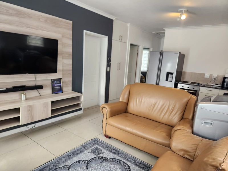Open-plan living area featuring tiled flooring, a modern built-in media unit, and an integrated kitchen space with built-in cabinetry and appliances.