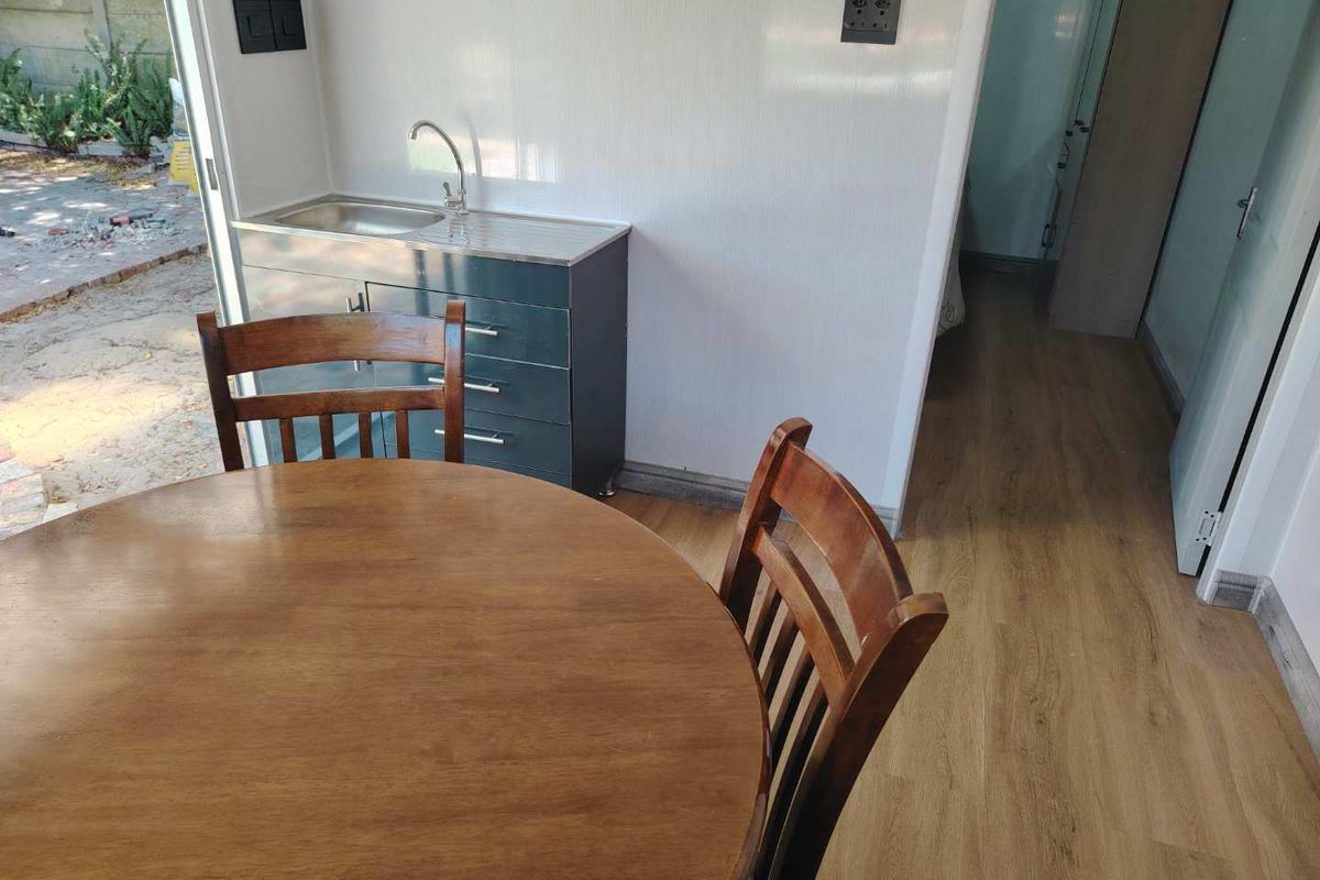 A compact kitchen area featuring a stainless steel sink and built-in cabinetry, with direct access to an outdoor space through a sliding glass door.